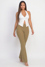 Woman wearing a white halter top and olive green flared pants on a white background