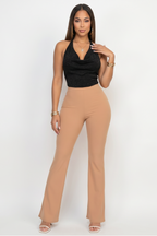 Woman wearing a black halter top and tan high-waisted pants on a white background