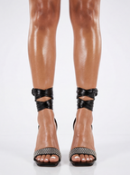 Black high-heeled sandals with decorative straps worn by a person on a white background