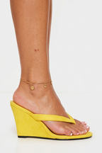 Yellow wedge sandals worn by a person on a white background