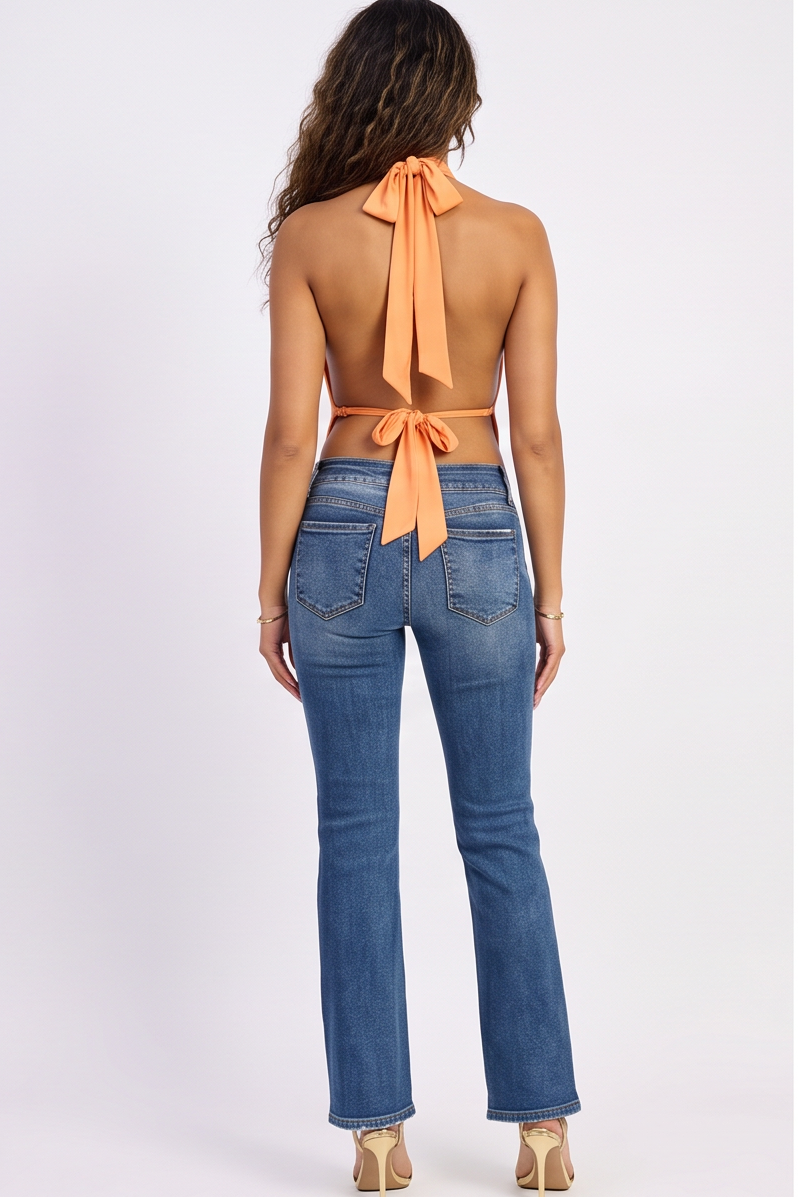 Woman wearing an orange halter top with a bow and blue jeans on a white background