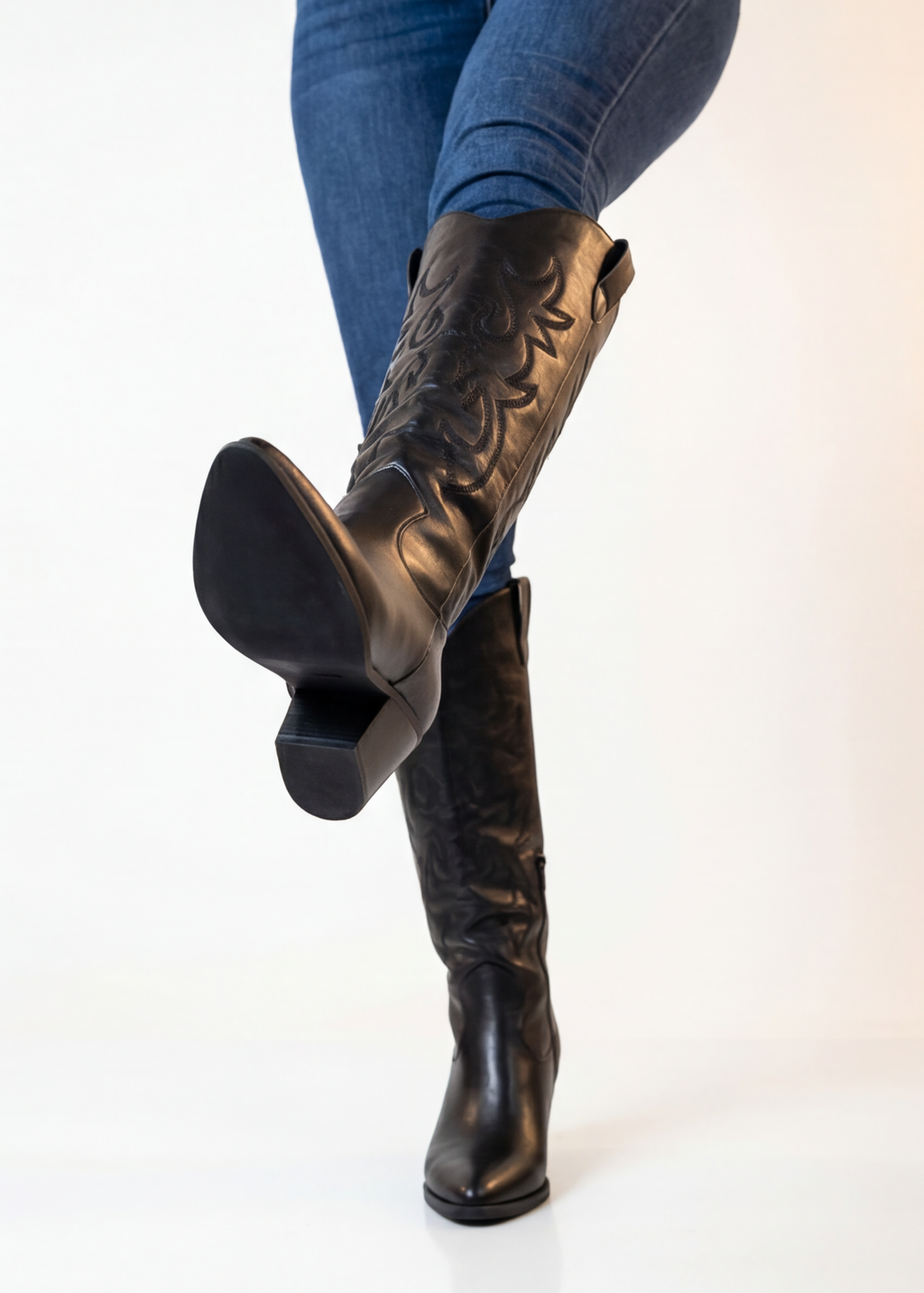 Black knee-high boots worn with blue jeans on a white background