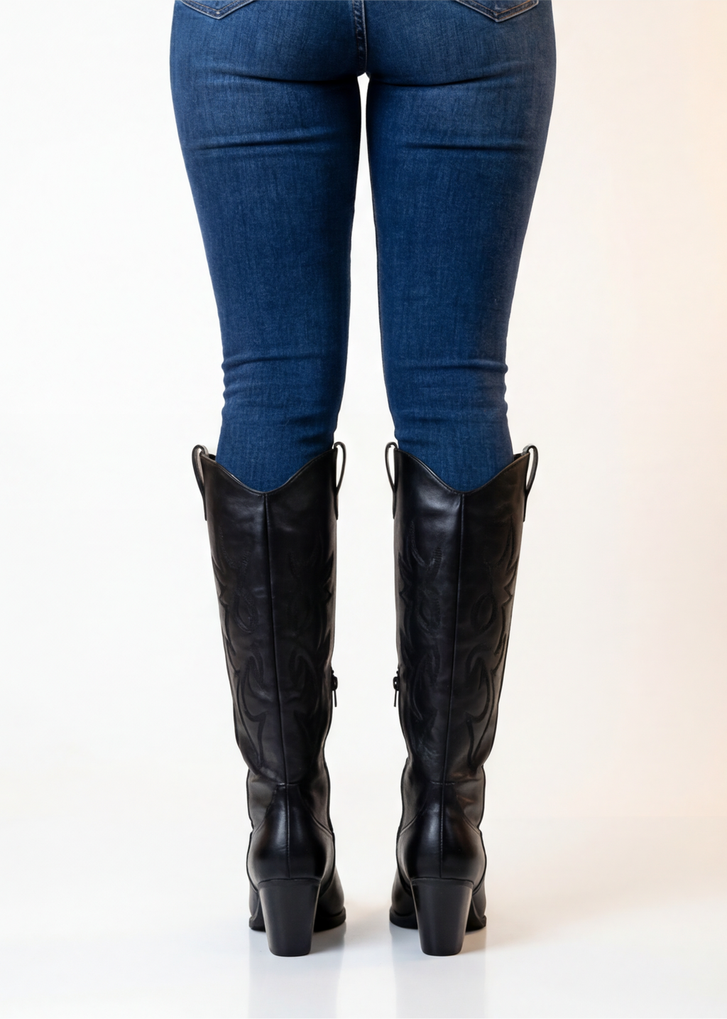 Black knee-high boots worn with blue jeans on a white background
