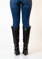 Black knee-high boots worn with blue jeans on a white background