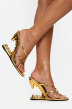 Gold high-heeled sandals with unique designs worn by a person on a white background