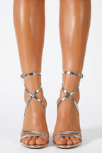 High-heeled sandals with metallic straps worn by a person on a white background