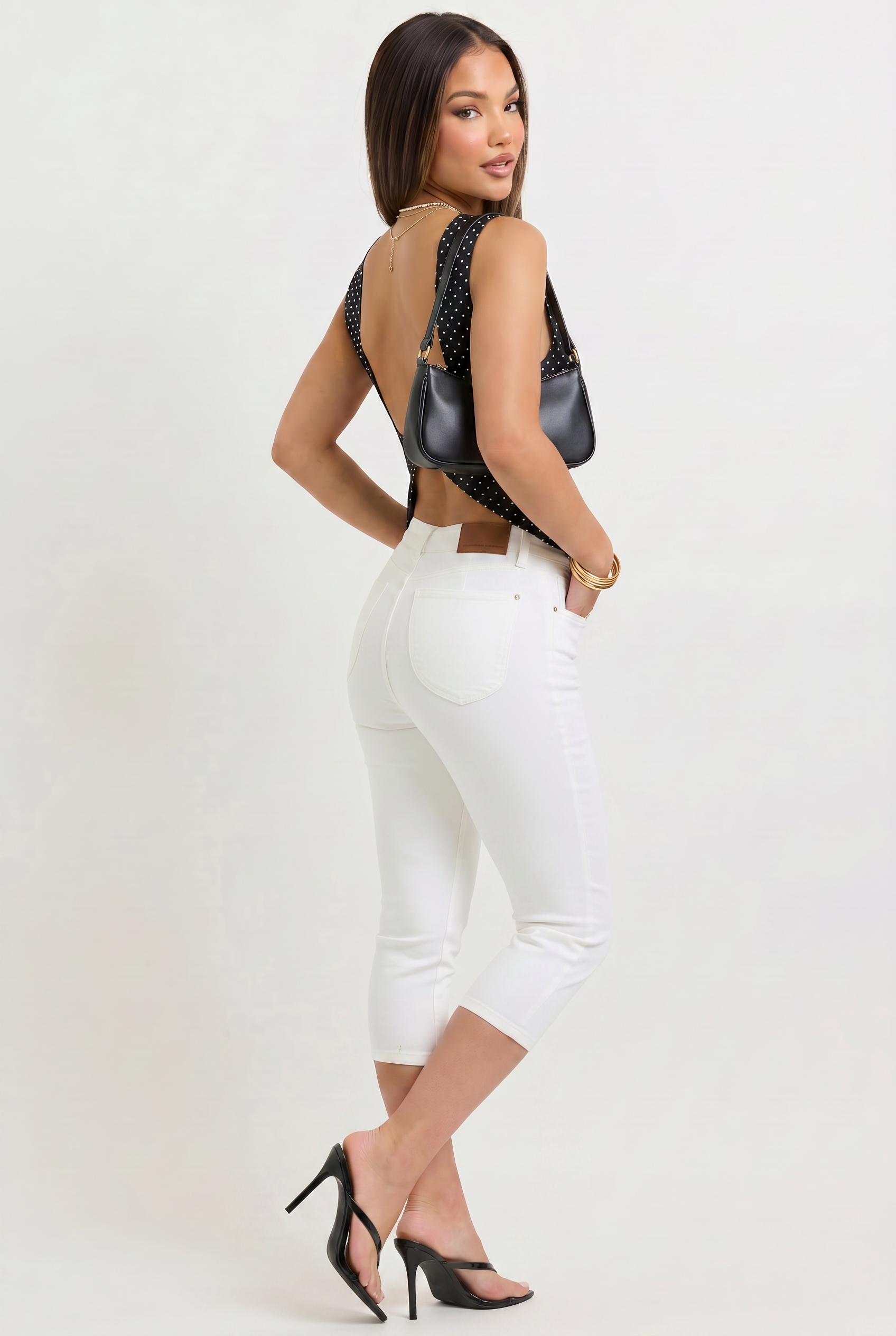 Woman wearing a black open-back top and white pants on a white background